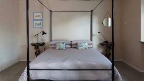 Una cama con dosel, ropa de cama a rayas, un espejo redondo y dos cuadros en la pared.
