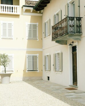 A building with multiple windows, a balcony with ornate metal railings, and a small tree in a planter. - Casa Fogliati - Alloggio 1 (San Bovo)