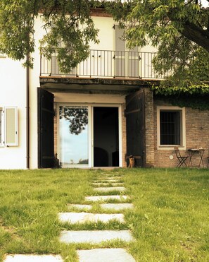 A house with a front door, a small patio with a table and chairs, and a stone pathway leading to the entrance. - Casa Fogliati - Alloggio 1 (San Bovo)