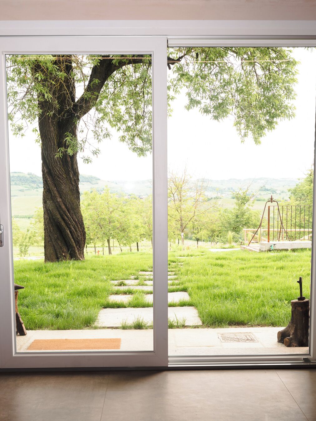 A door leading to a grassy outdoor area with a large tree and a swing set.