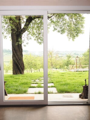 A door leading to a grassy outdoor area with a large tree and a swing set. - Casa Fogliati - Alloggio 1 (San Bovo)