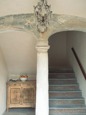 A staircase with a wooden handrail, a white column, and a bowl of fruit on a wooden cabinet. - Casa Fogliati - Alloggio 1 (San Bovo)