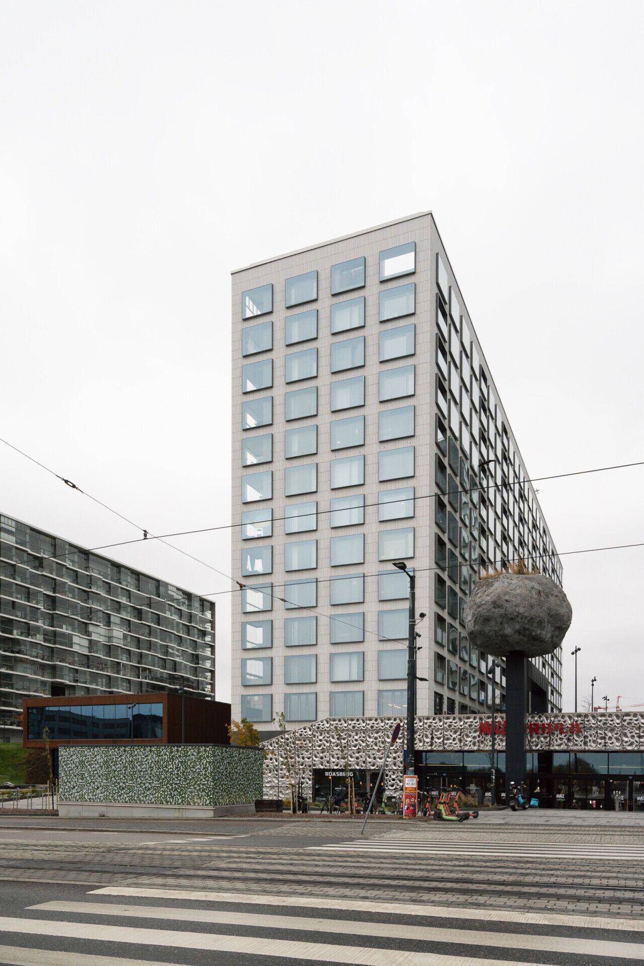 En moderne bygning med et vinduesgitter og en markant, kugleformet struktur foran.