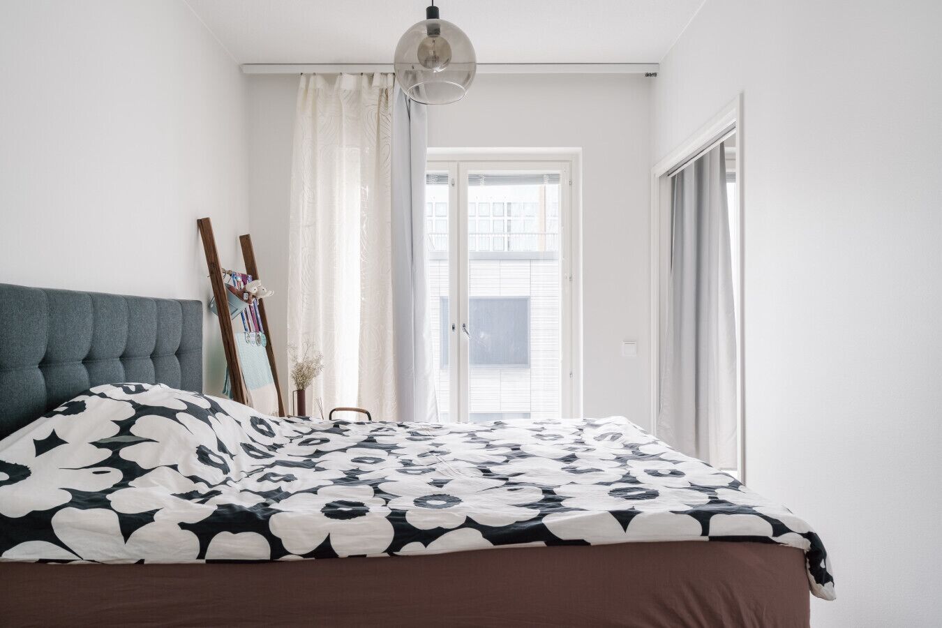 Ein Schlafzimmer mit Bett, Deckenlampe, Fenster mit Vorhängen und einer Tür.
