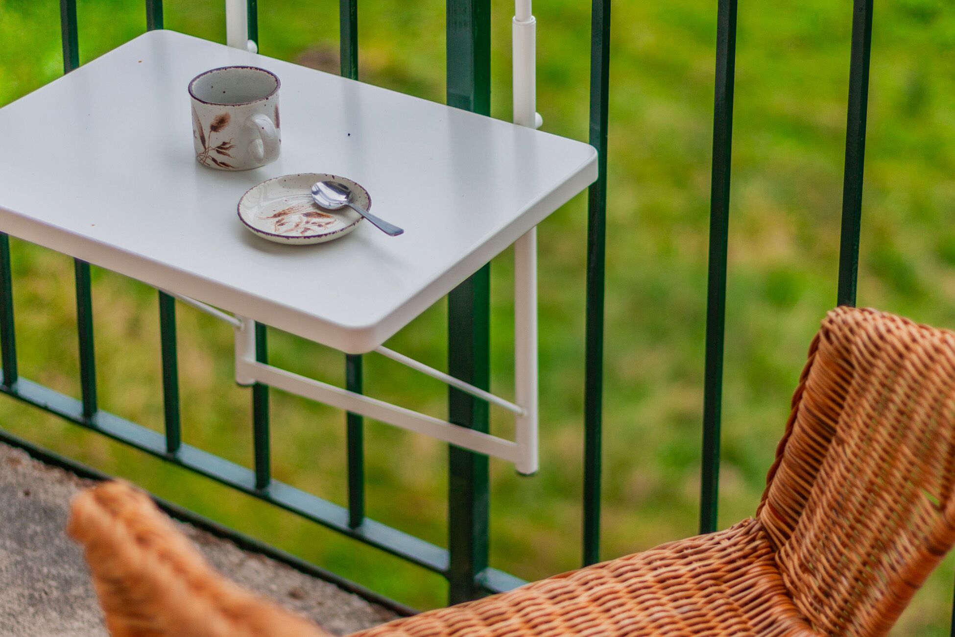 Ein Korbstuhl und ein kleiner weißer Tisch mit einer Tasse und einem Untertasse.