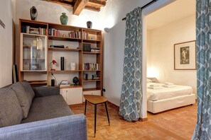Un salon comprenant un canapé, une petite table, une bibliothèque et un lit agrémenté d’un rideau à motifs.