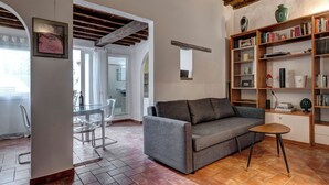 Uma sala de estar com sofá, uma mesinha, estante e piso de azulejos.