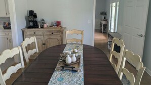 A dining area with a wooden table, chairs, a chandelier, and a kitchen in the background. - Fully Equipped Brandon Home — Comfortable & Convenient off Hwy 471 (Brandon)