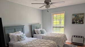 A bedroom with two beds, a ceiling fan, a window with blinds, a painting, and a walking aid. - Fully Equipped Brandon Home — Comfortable & Convenient off Hwy 471 (Brandon)