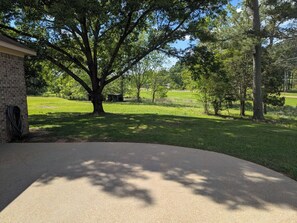 A paved driveway leading to a grassy area with trees, a brick building, and a clear sky.