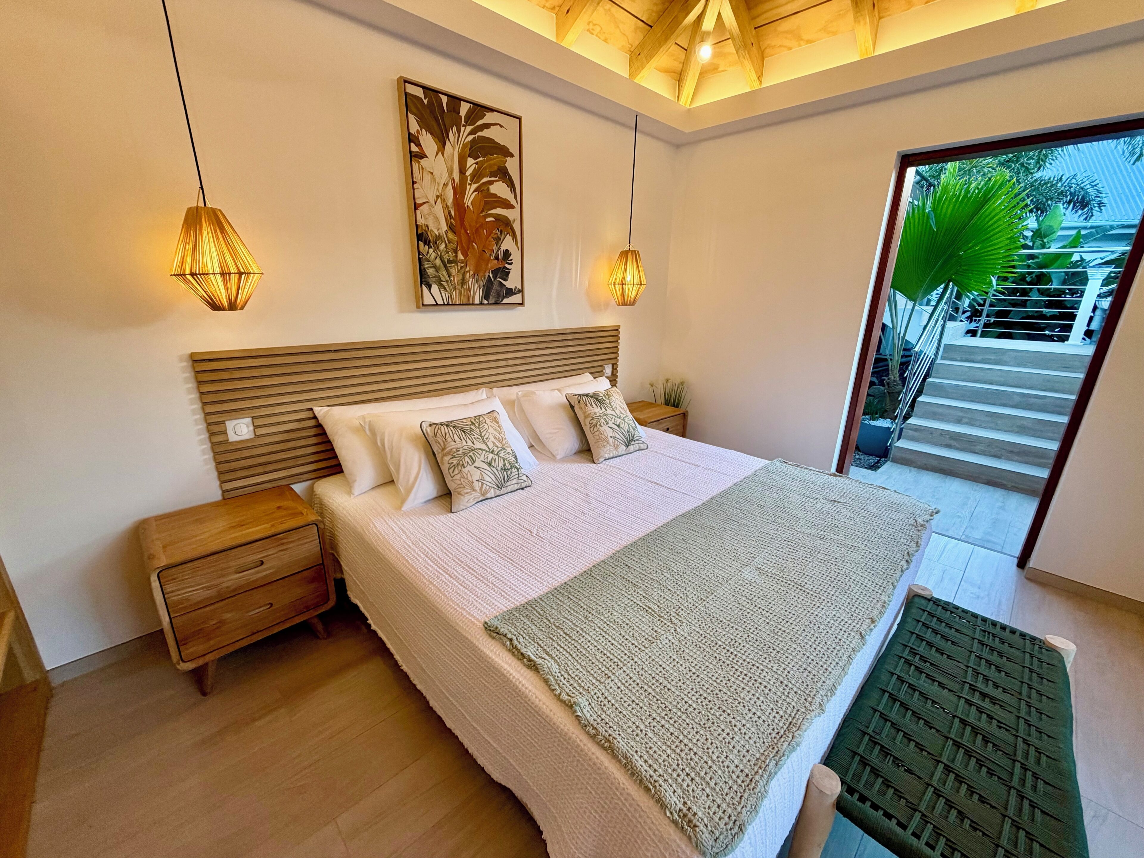 A bedroom with a bed, bedside tables, a wall-mounted artwork, and a view of a staircase leading outside.