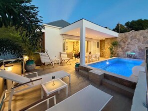 A modern outdoor pool area with a stone wall, lounge chairs, and a covered seating area. - Villa KOSY - sunset & beach on foot (Saint-Barthélemy)