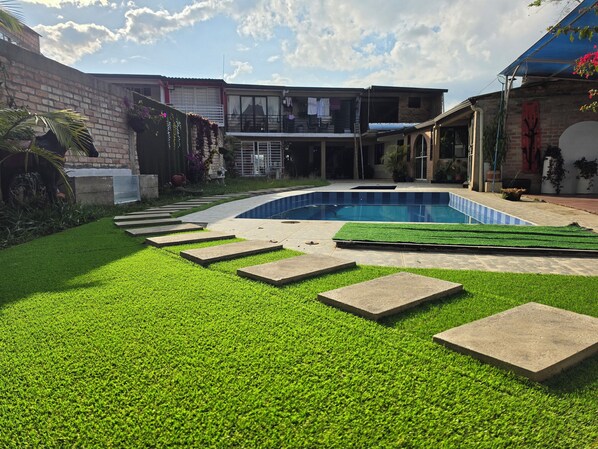 A backyard with a swimming pool, a brick wall, and a house with a balcony.