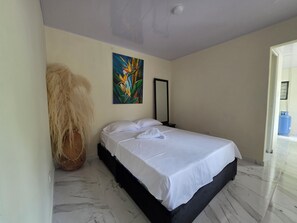 A bedroom with a bed, a painting, a mirror, and a large plant.