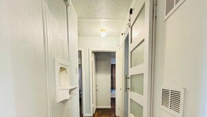 A narrow hallway with wooden flooring, white walls, and doors with vents. - 🏡 Heart of Abilene – Charming 3-Bedroom, 1-Bath Home ✨<br><br>Enjoy a cozy and inviting stay in this 3-bedroom, 1-bath home, perfectly located near restaurants, shopping, and local attractions 🍽️🛍️. (Abilene)