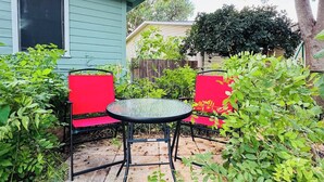 A patio with a round table and two red chairs, surrounded by greenery and a house in the background. - 🏡 Heart of Abilene – Charming 3-Bedroom, 1-Bath Home ✨<br><br>Enjoy a cozy and inviting stay in this 3-bedroom, 1-bath home, perfectly located near restaurants, shopping, and local attractions 🍽️🛍️. (Abilene)