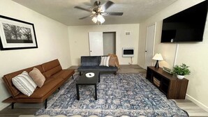 A living room with a brown sofa, a blue patterned rug, a ceiling fan, a TV, and a small table with a lamp. - 🏡 Spacious Stay on Bridge – 4BR / 2BA<br><br>Comfortable 4-bedroom, 2-bath home perfect for families or groups, with bright living areas, a full kitchen, and a convenient Abilene location. 🌟 (Abilene)