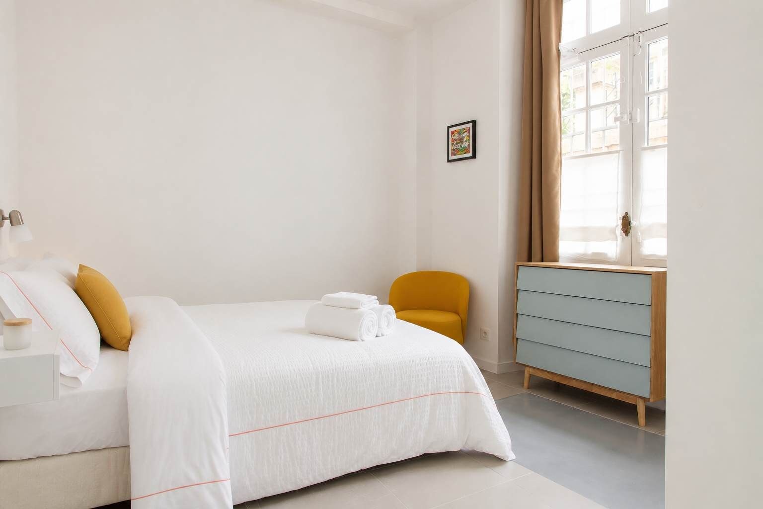 A hotel room with a bed, a chair, a dresser, and a window with curtains.