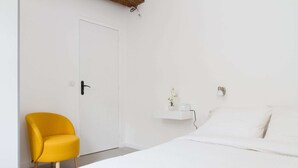 Ein Schlafzimmer mit einem Bett, einer weißen Tür, einem gelben Stuhl und einem kleinen, weißen Regal mit einer Pflanze.