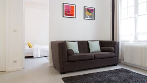 Ein modernes Wohnzimmer mit einer braunen Couch, zwei gerahmten Kunstwerken an der Wand, einem großen Fenster und einer Tür zu einem anderen Raum.
