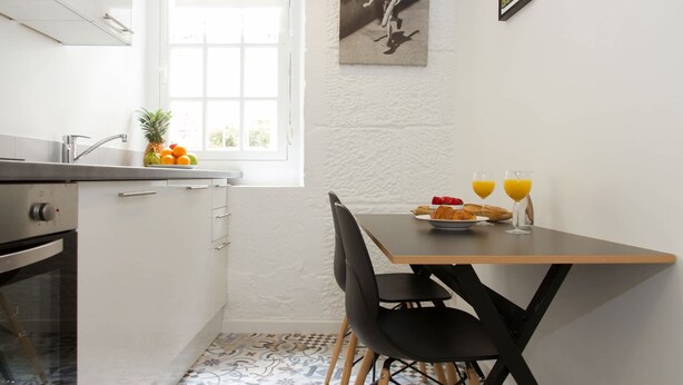 Eine kompakte Küche mit Fenster, einem Esstisch mit Stühlen und einer Frühstücksecke mit Obst und Saft.