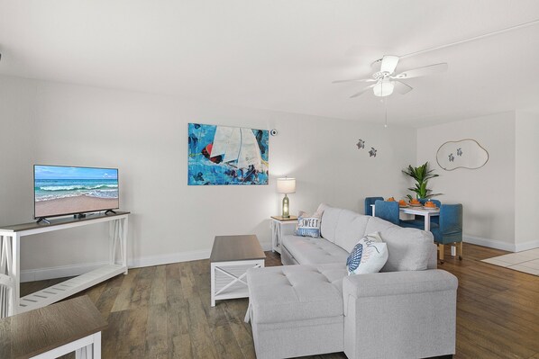 Ein Wohnzimmer mit Fernseher, Gemälde, Deckenventilator und einer Couch.