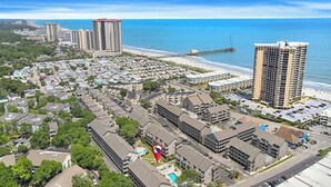 Vue aérienne d’une zone urbaine côtière, avec des immeubles de grande hauteur, une plage et un port de plaisance.