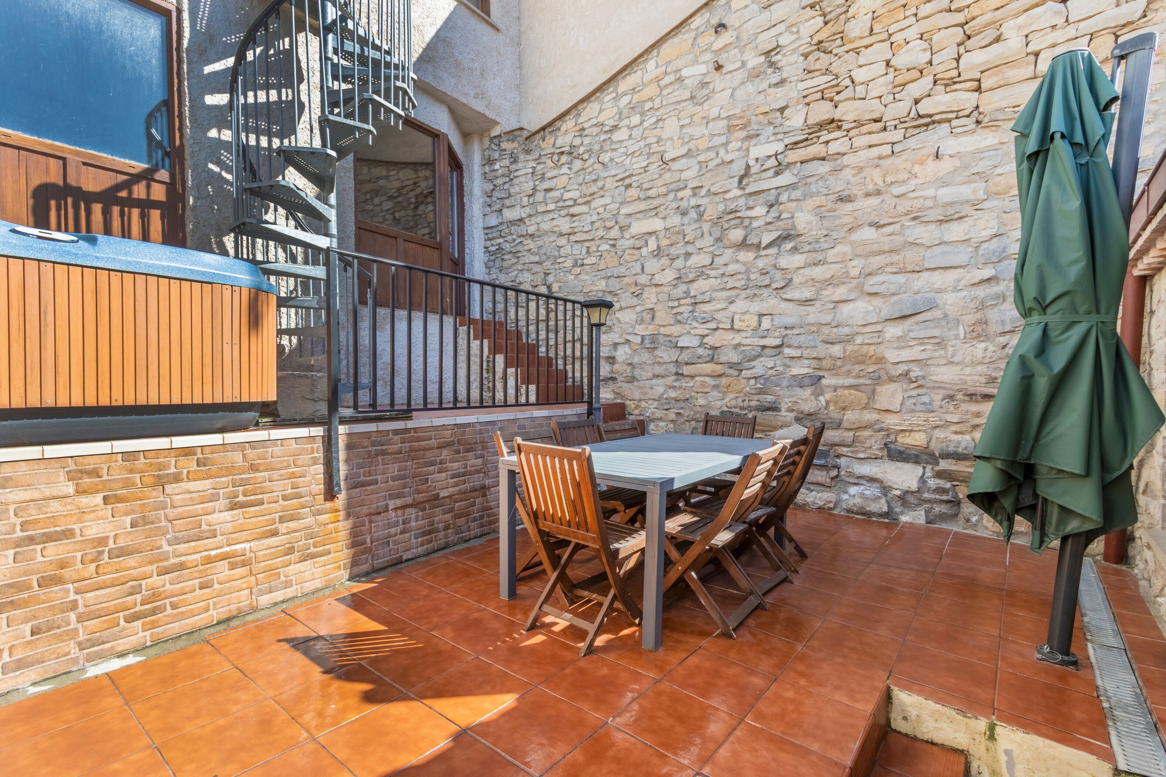 A patio with a table and chairs, a covered outdoor seating area, a stone wall, and a staircase.
