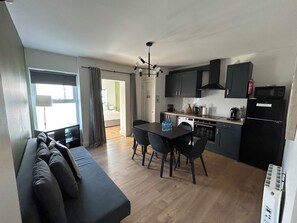 A compact living space with a sofa, dining table, chairs, a kitchenette, and a view through an open door. - Dublin citycenter 3 Bedrooms Apartment (Dublin)