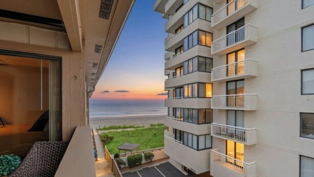 A modern hotel with a balcony overlooking a beach at sunset. - Crescent Villas 302- 2 Bedroom Condo- Pool (North Myrtle Beach)