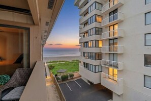Ein modernes Hotel mit Balkon und Blick auf einen Strand bei Sonnenuntergang.