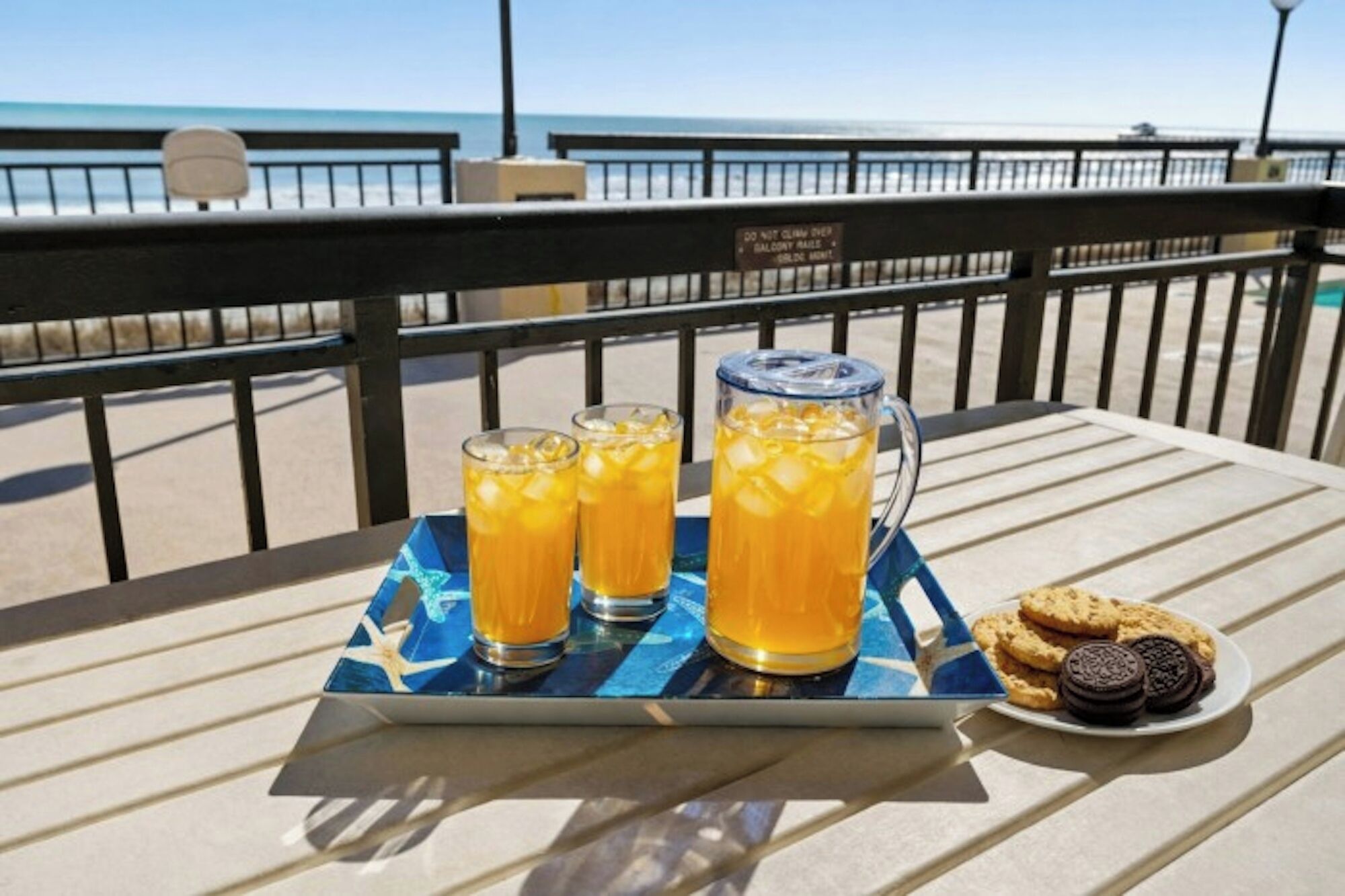 Una mesa con una bandeja que contiene tres vasos de bebida de naranja y una jarra, junto a un plato con galletas y dos galletas Oreo.