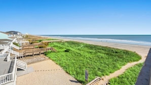 Blick auf einen Strand mit einer Rasenfläche, Holzstegen und blauem Himmel.