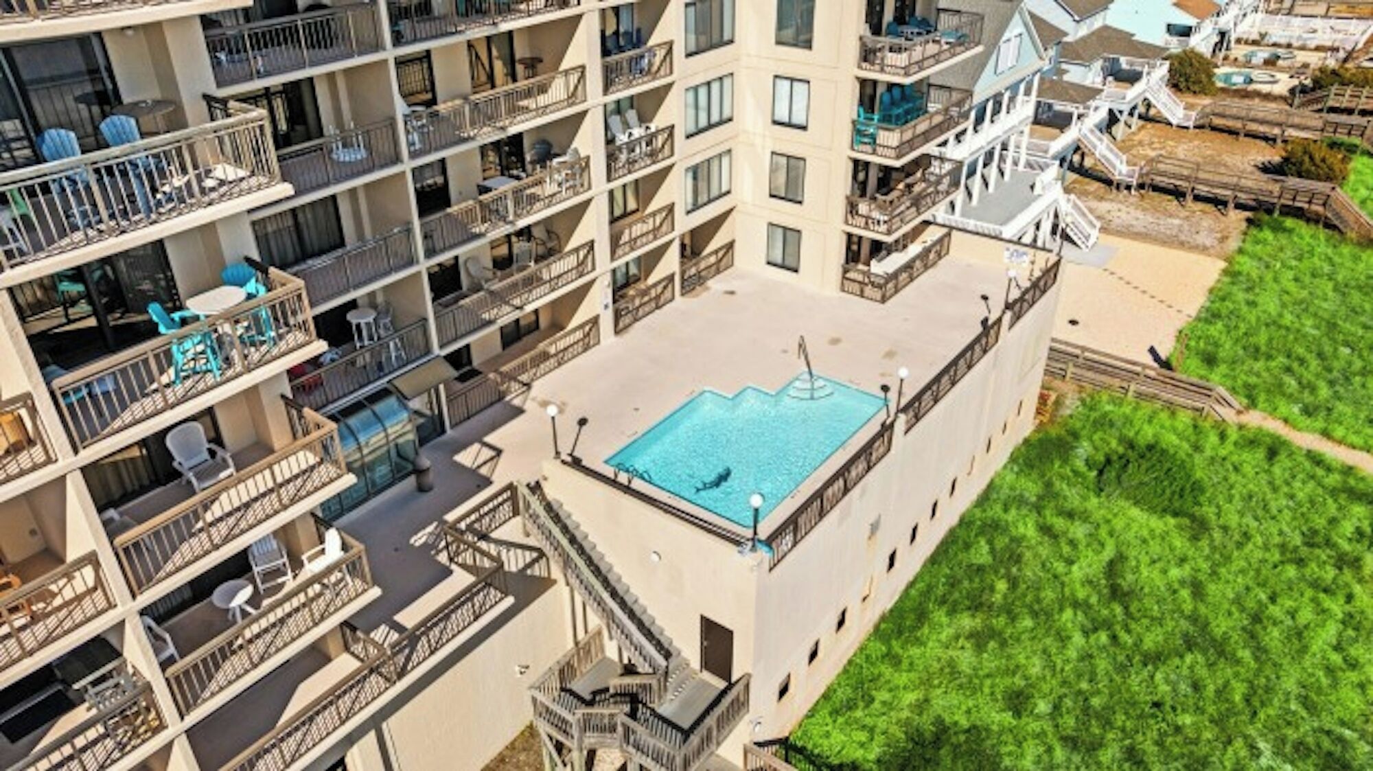 Un hotel a più piani con balconi, una piscina sul tetto e una zona verde.