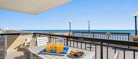Un balcón con una mesa preparada para el desayuno, con vistas a la playa y al mar.