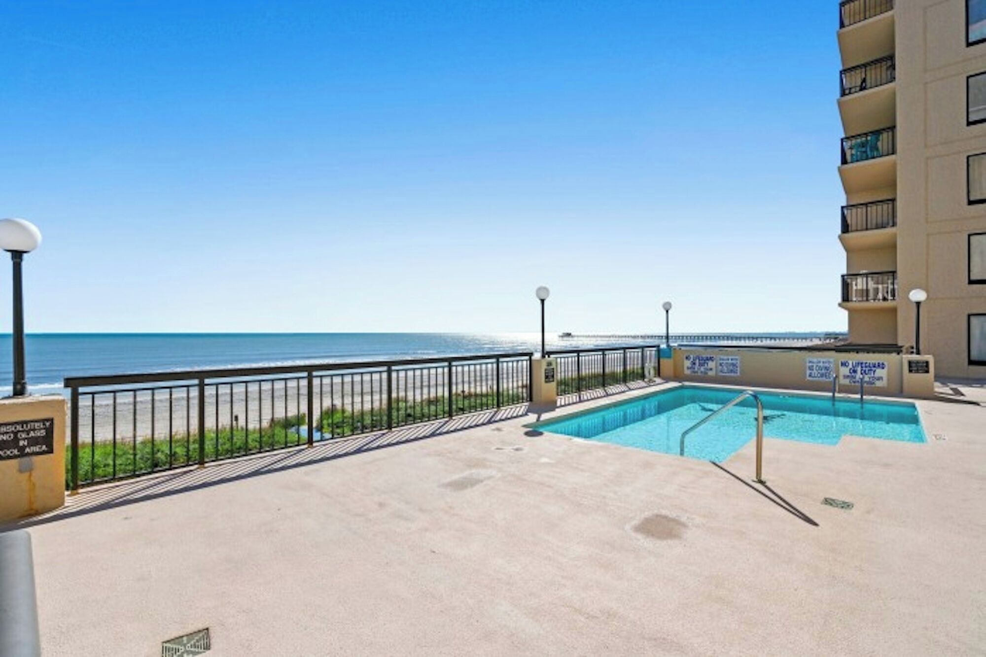 Une piscine sur le toit, offrant une vue sur l’océan, entourée d’une clôture et bordée d’un immeuble doté de balcons.
