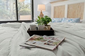 A neatly made bed with a magazine, a potted plant, and a lamp on a bedside table. - Ocean View Tower II 1B- Short Walk To Beach-Pool (Myrtle Beach)