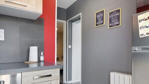 Een moderne keuken met grijze tegels, een rode accentmuur, houten kastjes, een inbouwvaatwasser en een prullenbak.