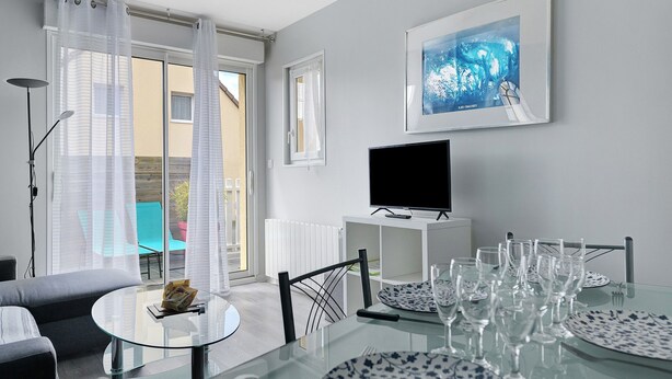 Een moderne woonkamer met een glazen eettafel, een bank, een televisie en een schilderij aan de muur.