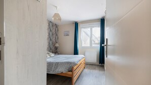 Una camera da letto con un letto, un comodino, una lampada, una finestra con tende e un termosifone.