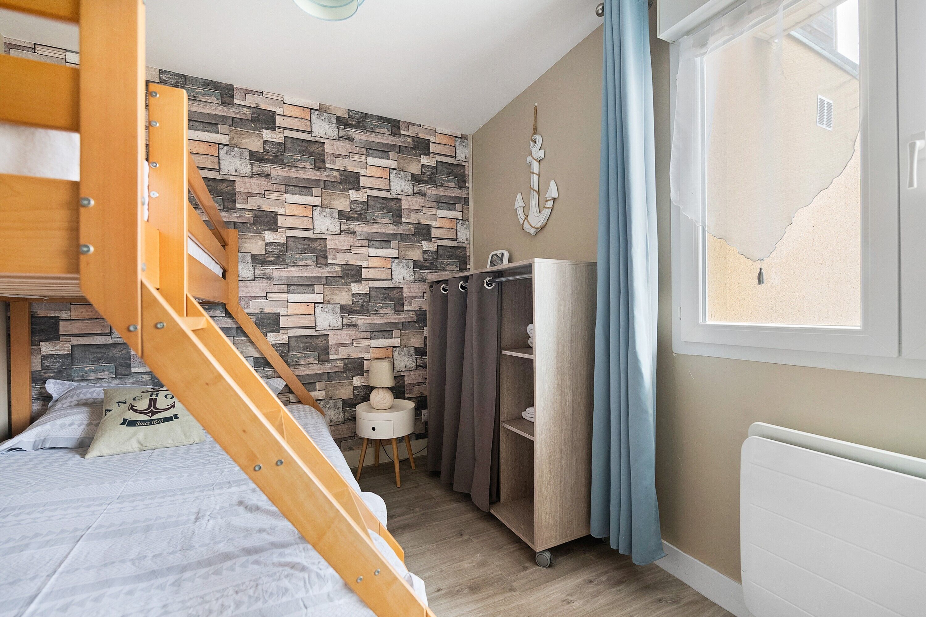 Un dormitorio con una litera, una pared de diseño de piedra, un radiador blanco y una ventana con cortinas.