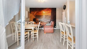 Zona pranzo con tavolo e sedie, un divano in pelle e un affresco raffigurante un tramonto sull'oceano.