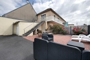 Ein Gebäude mit einer Treppe, die zu einem Balkon führt, Sitzgelegenheiten im Freien und einem Blumengarten.