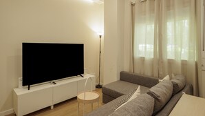 Una sala de estar moderna con un televisor de pantalla plana, un sofá, una mesita redonda y una lámpara de pie.