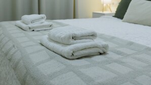 Una cama bien tendida con toallas blancas dobladas y un cojín verde.