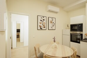 Une cuisine équipée d’une table à manger, de chaises, d’un réfrigérateur, d’un four et de deux climatiseurs fixés au mur.