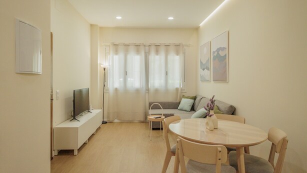 A modern living room with a flat-screen TV, a dining table with chairs, a sofa, and a small side table. - Private Jacuzzi Apartment in Central Seville – 4 Guests (Sevilla)