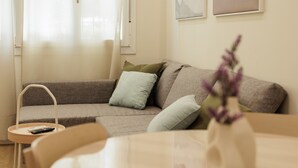 A modern living room with a sofa, a small side table, a remote control, and a vase with flowers. - Private Jacuzzi Apartment in Central Seville – 4 Guests (Sevilla)