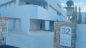 Edifici modern de color blanc amb un disseny arquitectònic únic, una paret de pedra amb un símbol de número i un cel clar.