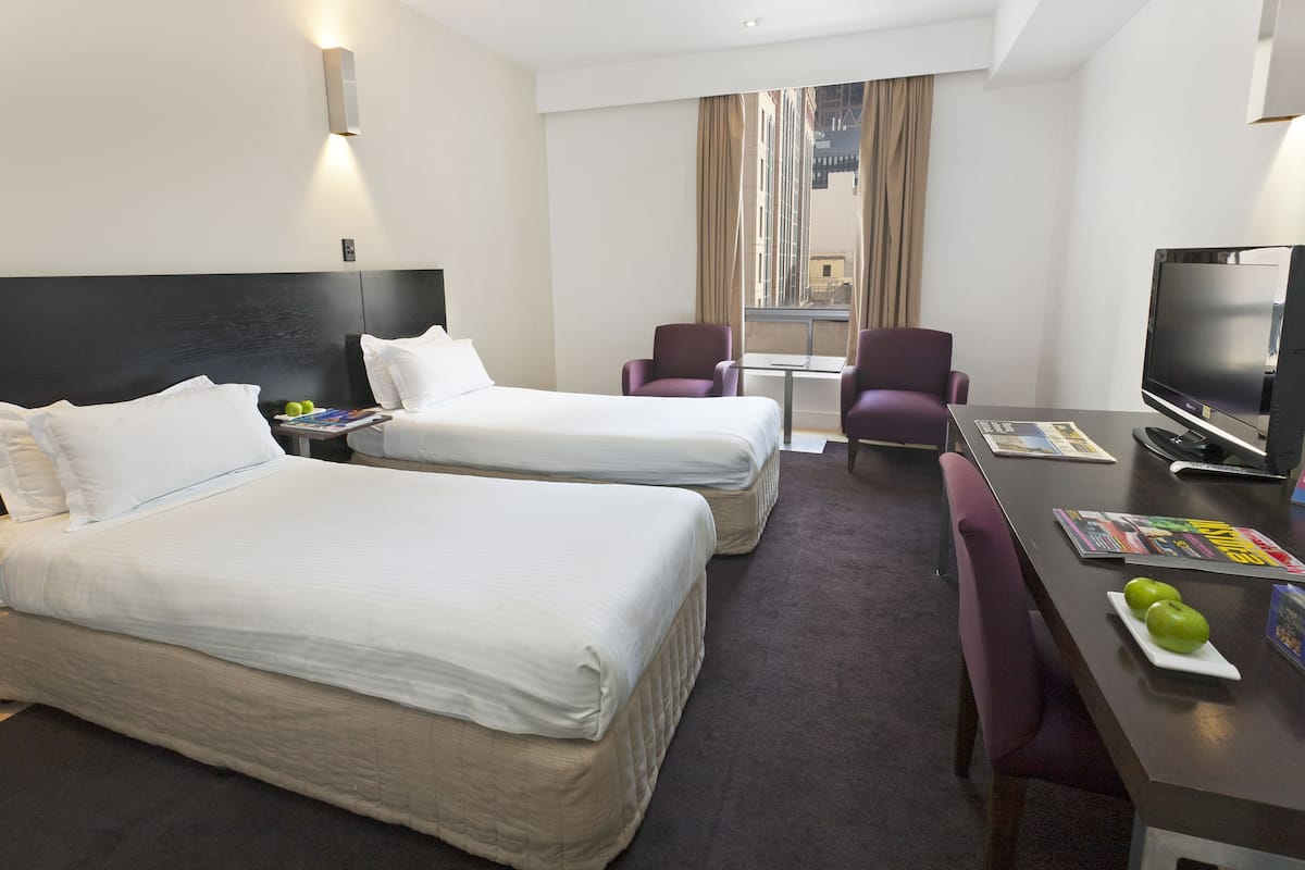 A hotel room with two beds, a desk with a TV, and a window with curtains.